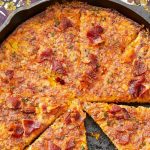 Golden brown eggless bacon cornbread baked in cast iron skillet with crispy edges and bacon pieces visible throughout