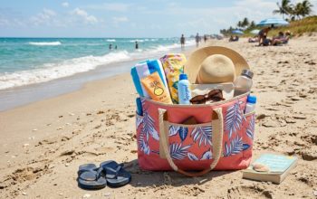 Large waterproof tote bag packed with towels, sunscreen, and beach essentials sitting on sandy shore near the water