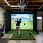 A home golf simulator setup in a garage with a large impact screen, projector, and hitting mat