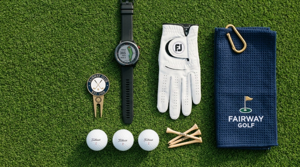 Flat lay of stylish golf essentials including a GPS watch, enamel ball marker, microfiber towel, and premium glove on a green background