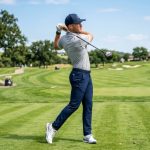 Modern golfer wearing trendy golf gear including a structured cap, leather glove, and spikeless shoes on a sunny fairway
