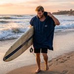 A surfer drying off with a blue surf poncho on a sunny California beach.