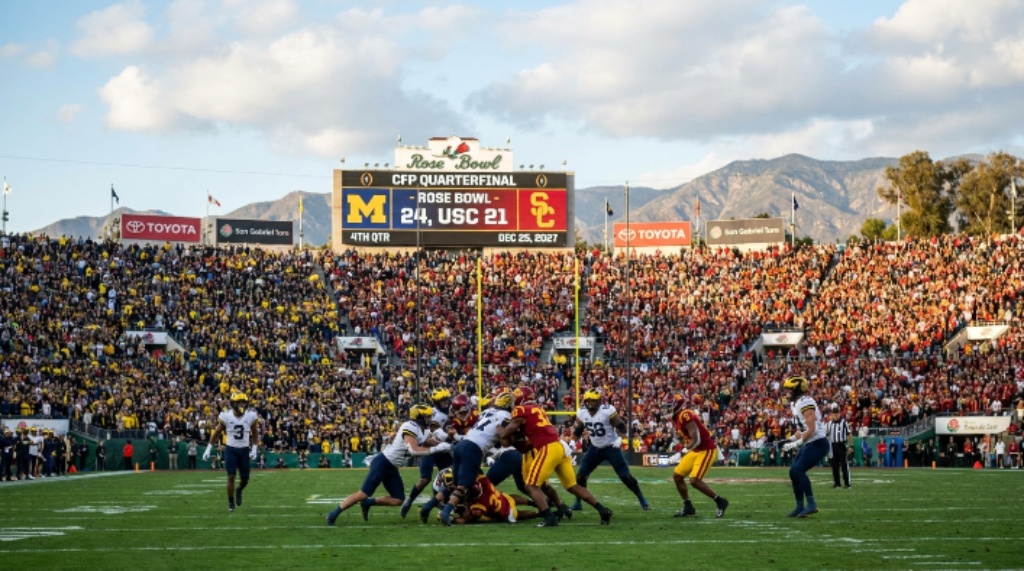 College football players competing on the Bermuda grass field of the Rose Bowl Stadium during the 2027 CFP Quarterfinal game in Pasadena, California, with a full crowd of nearly 90,000 fans surrounding them